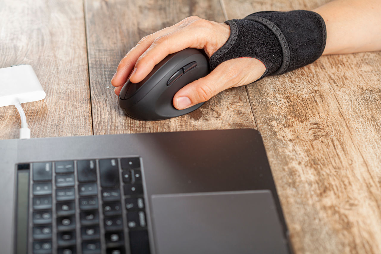 Chronic trauma to the wrist joint  in people using computer mouse may lead to disorders that cause inflammation and pain. A woman working on desk uses wrist support brace and ergonomic vertical mouse,Chronic trauma to the wrist joint  in people using computer mous