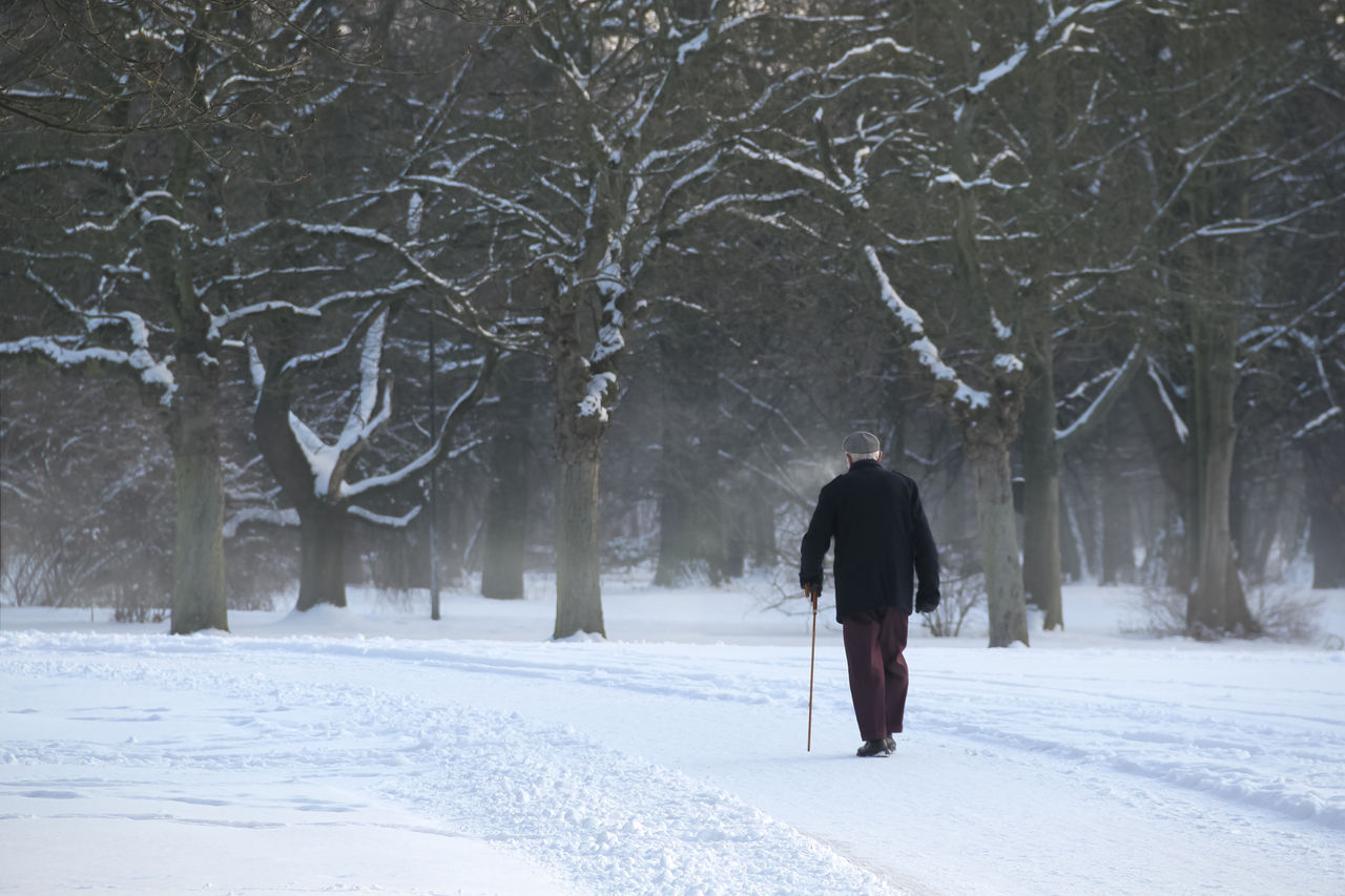 Einsamer alter Mann läuft am Gehstock durch den Winter