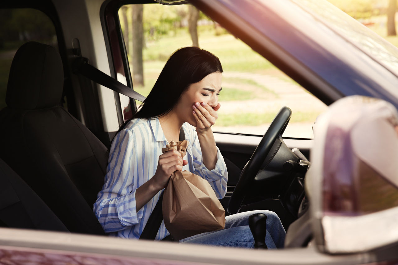 Young woman with paper bag suffering from nausea in car