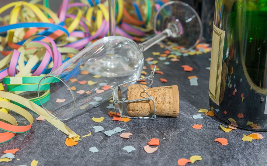 Champagner Glas und Flasche mit Faschingsdekoration auf einer Schieferplatte 